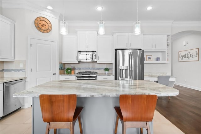 kitchen featuring crown molding, light stone countertops, a kitchen island, white cabinetry, and stainless steel appliances