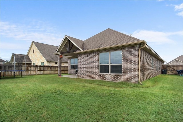 back of house featuring a trampoline and a yard