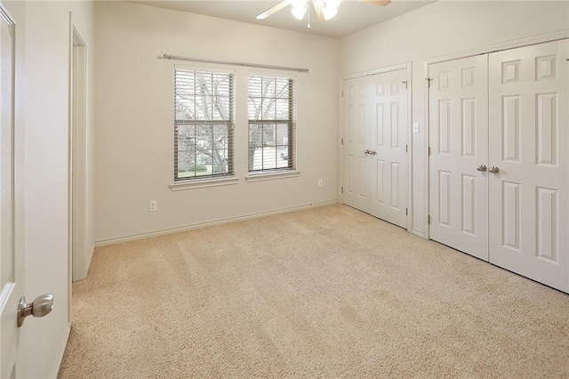 unfurnished bedroom with ceiling fan, two closets, and light carpet