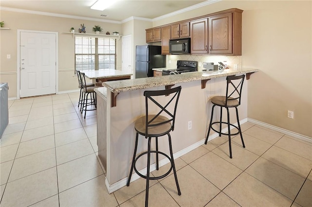 kitchen with a breakfast bar area, light tile patterned floors, and black appliances