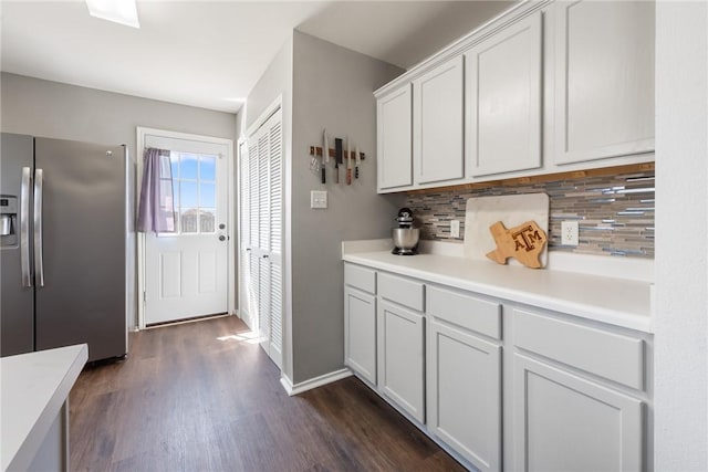 kitchen featuring backsplash, baseboards, light countertops, stainless steel refrigerator with ice dispenser, and dark wood-style floors