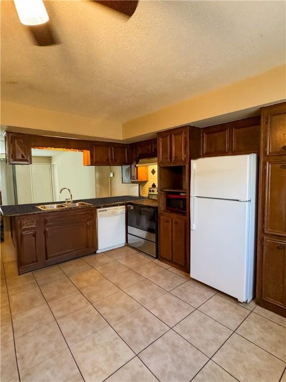 kitchen with a sink, dark countertops, a textured ceiling, white appliances, and light tile patterned flooring