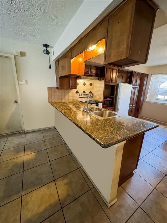 kitchen with tile patterned floors, a sink, tasteful backsplash, freestanding refrigerator, and a peninsula