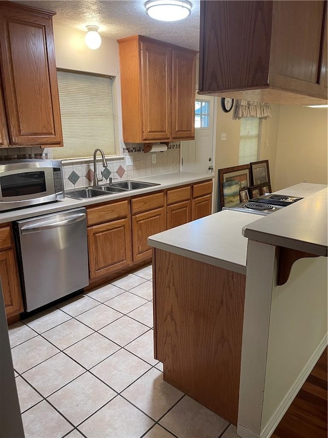 kitchen featuring sink, a textured ceiling, appliances with stainless steel finishes, tasteful backsplash, and light tile patterned flooring