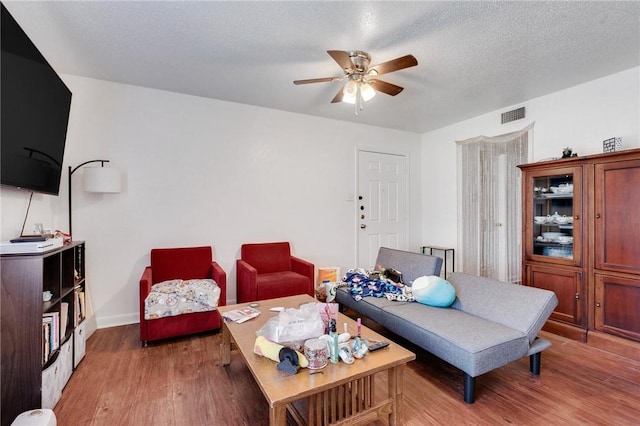 living area with a ceiling fan, baseboards, visible vents, a textured ceiling, and light wood-type flooring