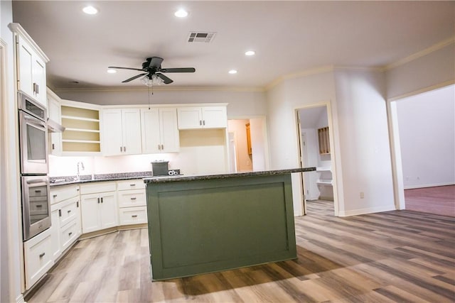 kitchen with ornamental molding, light wood-type flooring, a kitchen island, and white cabinets