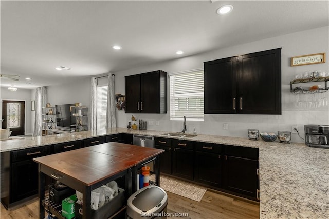 kitchen with light wood-type flooring, light stone counters, stainless steel dishwasher, and sink