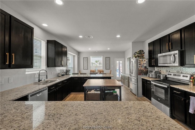 kitchen featuring light stone countertops, sink, stainless steel appliances, tasteful backsplash, and light hardwood / wood-style flooring