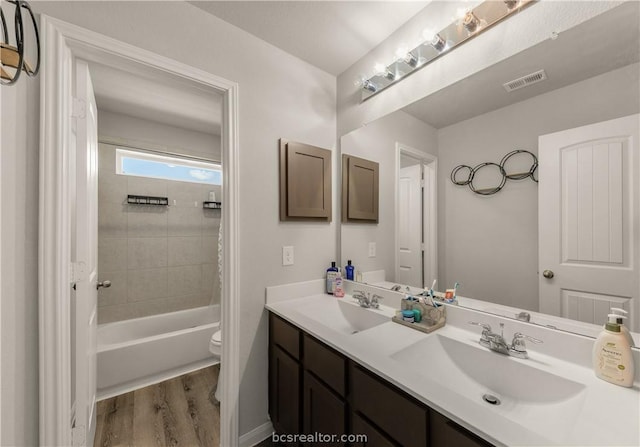 full bathroom featuring hardwood / wood-style flooring, vanity, toilet, and tiled shower / bath