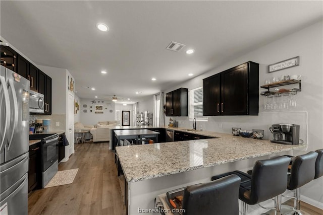 kitchen with light hardwood / wood-style floors, a kitchen bar, kitchen peninsula, and appliances with stainless steel finishes