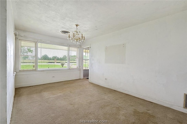 carpeted empty room featuring a chandelier and a textured ceiling