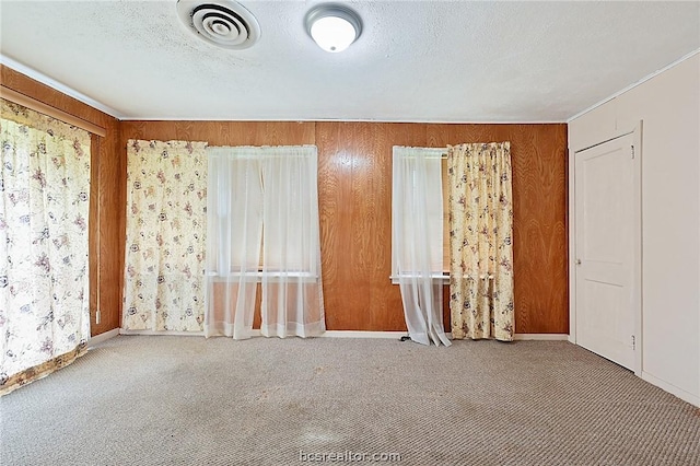 carpeted spare room with a textured ceiling and wood walls