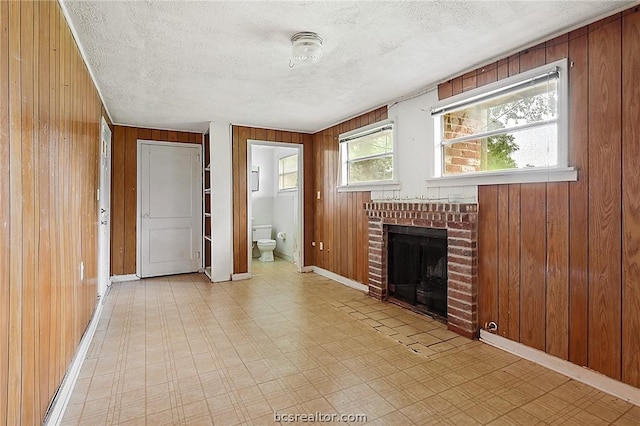 unfurnished living room with a fireplace, a textured ceiling, and wooden walls