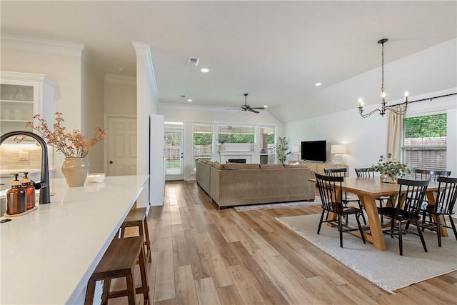 dining space featuring visible vents, ornamental molding, a fireplace, light wood-style floors, and ceiling fan with notable chandelier