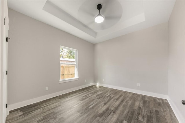 unfurnished room with a raised ceiling, ceiling fan, and dark hardwood / wood-style flooring