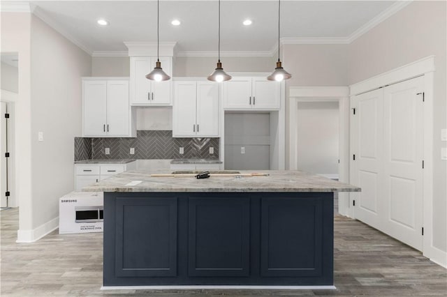 kitchen featuring light stone countertops, decorative light fixtures, a center island with sink, and white cabinets