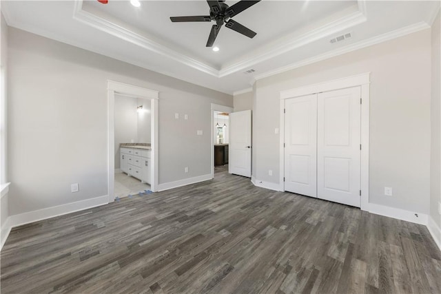 unfurnished bedroom featuring dark hardwood / wood-style flooring, a raised ceiling, ceiling fan, connected bathroom, and a closet