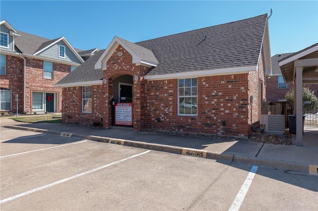 view of front of property with a shingled roof, brick siding, fence, and uncovered parking