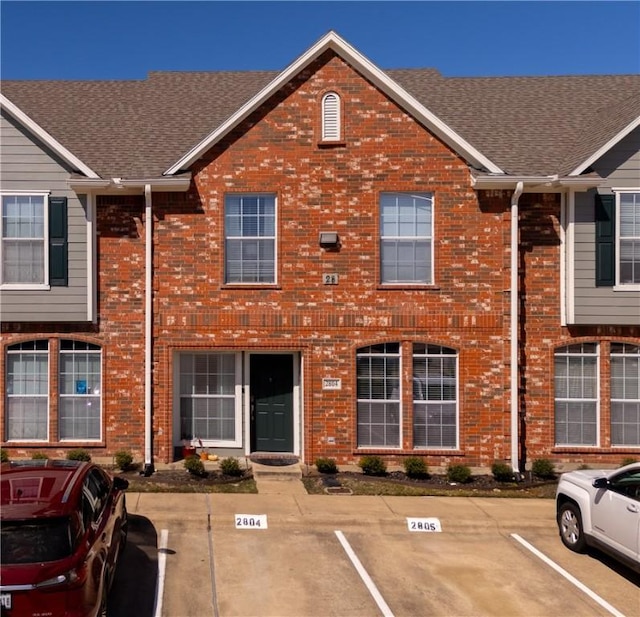 townhome / multi-family property featuring uncovered parking, brick siding, and a shingled roof