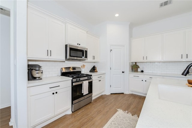 kitchen with stainless steel appliances, light countertops, visible vents, light wood-style floors, and a sink