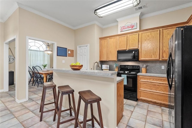 kitchen with backsplash, crown molding, black appliances, a breakfast bar area, and light tile patterned flooring