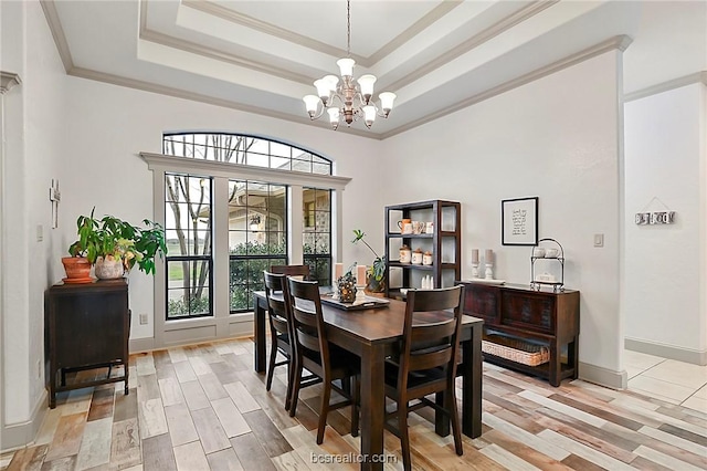 dining room with a notable chandelier, a raised ceiling, ornamental molding, and light hardwood / wood-style flooring