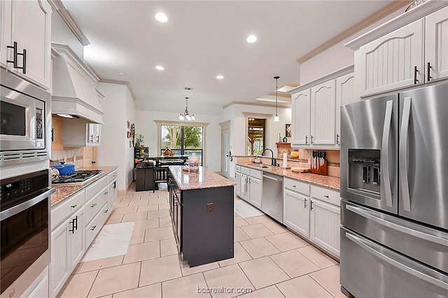 kitchen with light stone countertops, appliances with stainless steel finishes, sink, decorative light fixtures, and a center island