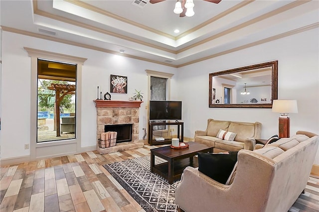 living room with light wood-type flooring, ornamental molding, a tray ceiling, ceiling fan, and a fireplace