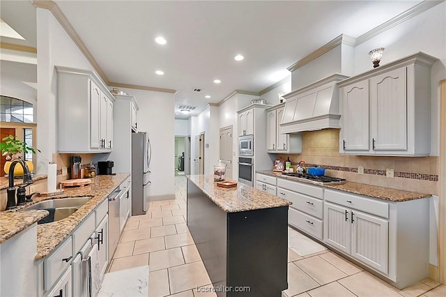 kitchen with appliances with stainless steel finishes, light stone counters, custom range hood, crown molding, and sink