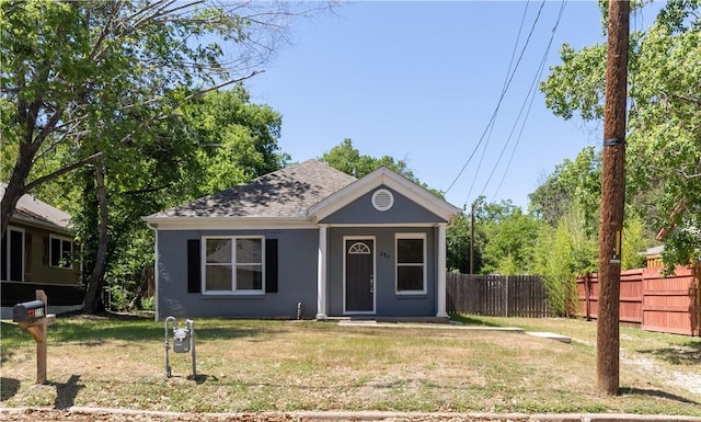 view of front of house with a front yard, roof with shingles, and fence