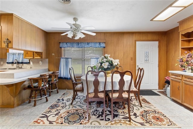 dining room featuring light tile patterned flooring, ceiling fan, wood walls, and sink