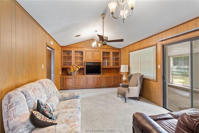 carpeted living room featuring ceiling fan with notable chandelier, lofted ceiling, and wood walls