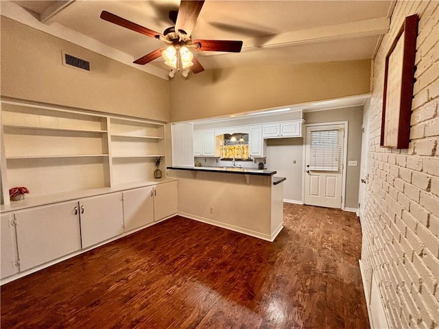 kitchen with lofted ceiling, white cabinetry, dark hardwood / wood-style flooring, brick wall, and kitchen peninsula