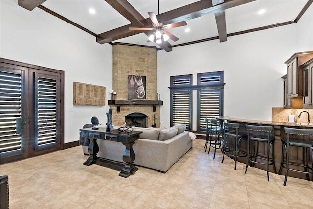 living room with beam ceiling, a fireplace, a towering ceiling, and ceiling fan