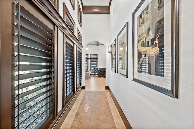 hall featuring arched walkways, a high ceiling, and baseboards