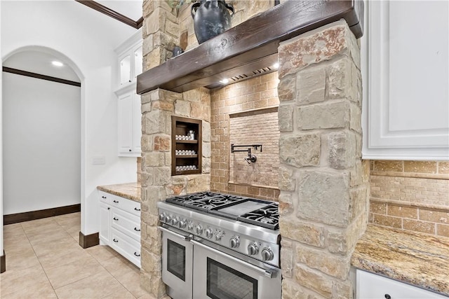 kitchen featuring light stone counters, range with two ovens, light tile patterned flooring, decorative backsplash, and white cabinetry