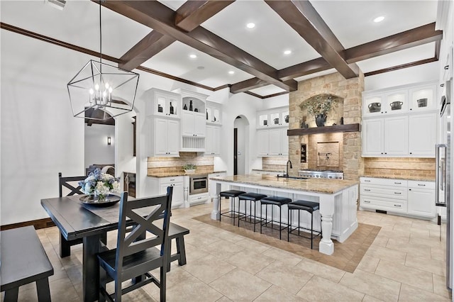 kitchen with a center island with sink, arched walkways, a sink, beamed ceiling, and tasteful backsplash