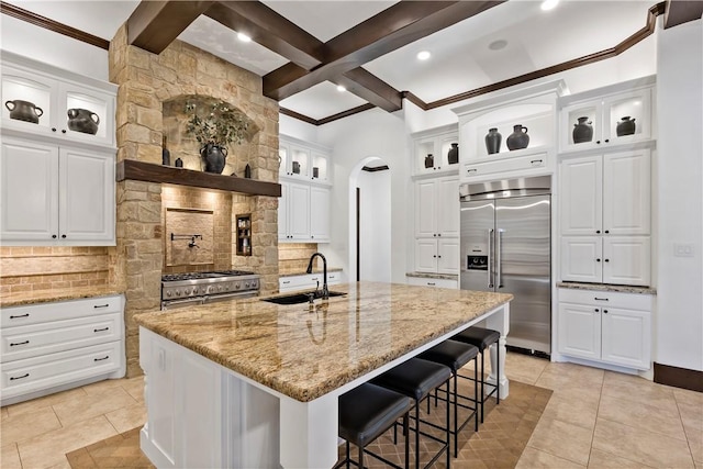 kitchen featuring a sink, light stone counters, arched walkways, decorative backsplash, and high end appliances