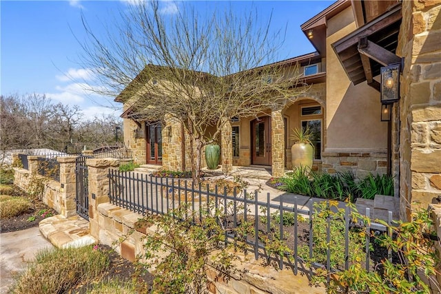 view of front of house featuring a gate, stone siding, a fenced front yard, and stucco siding