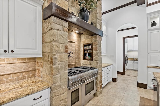 kitchen featuring range with two ovens, light stone counters, tasteful backsplash, and exhaust hood