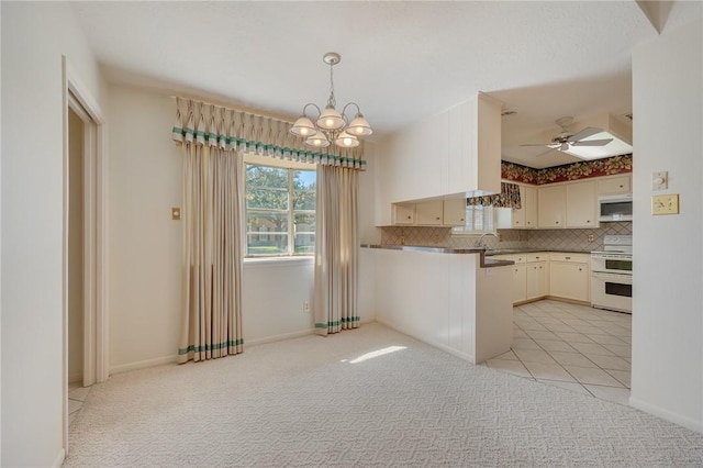 kitchen featuring decorative backsplash, white appliances, light colored carpet, ceiling fan with notable chandelier, and pendant lighting