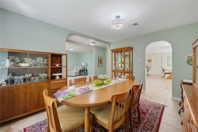 dining space featuring arched walkways, light tile patterned flooring, and visible vents