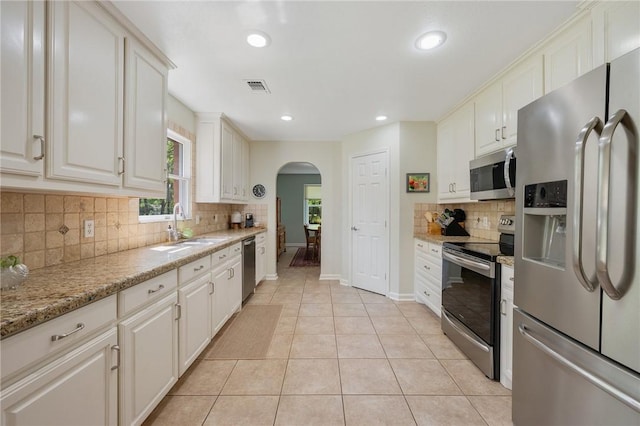 kitchen with visible vents, decorative backsplash, a sink, arched walkways, and appliances with stainless steel finishes