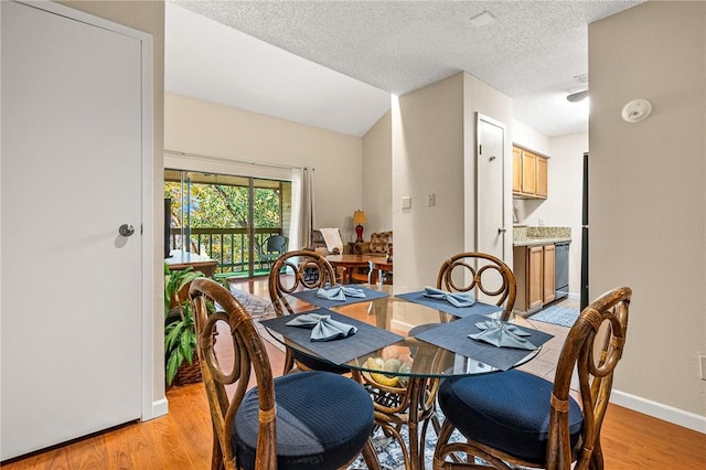 dining space with light hardwood / wood-style floors, lofted ceiling, and a textured ceiling