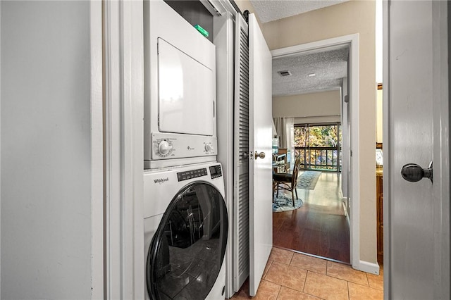 laundry room with a textured ceiling, light tile patterned floors, and stacked washer and clothes dryer