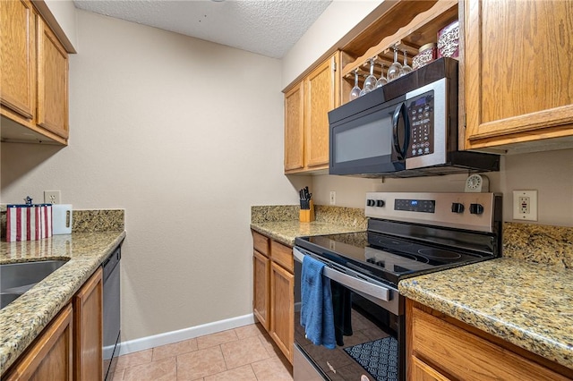 kitchen featuring appliances with stainless steel finishes, light tile patterned floors, a textured ceiling, and light stone counters