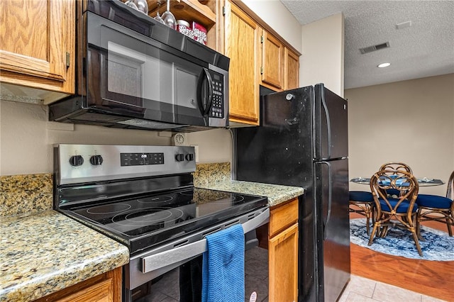 kitchen featuring light stone countertops, light tile patterned floors, black appliances, and a textured ceiling