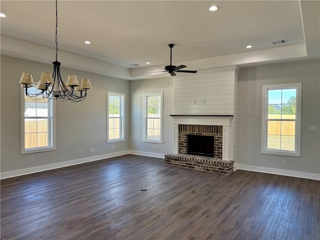 unfurnished living room with a raised ceiling, ceiling fan with notable chandelier, a brick fireplace, and dark hardwood / wood-style floors