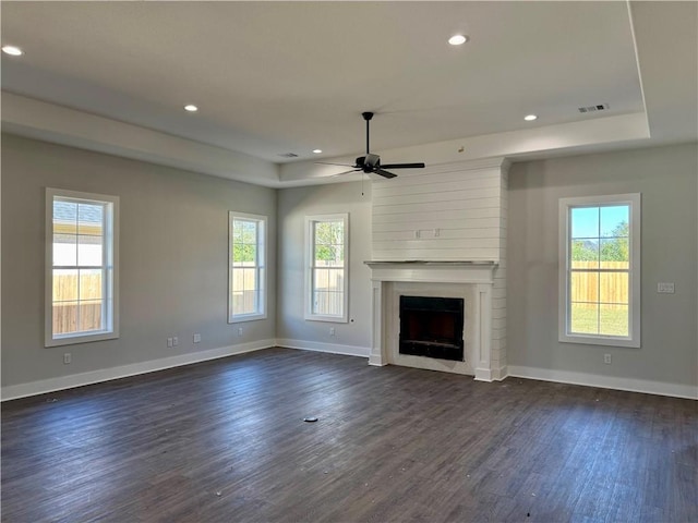 unfurnished living room featuring a raised ceiling, ceiling fan, a large fireplace, and dark wood-type flooring