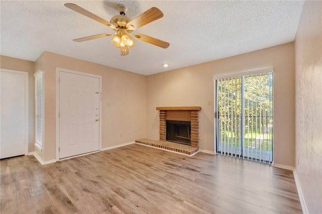 unfurnished living room featuring ceiling fan, light wood-type flooring, a textured ceiling, and a brick fireplace